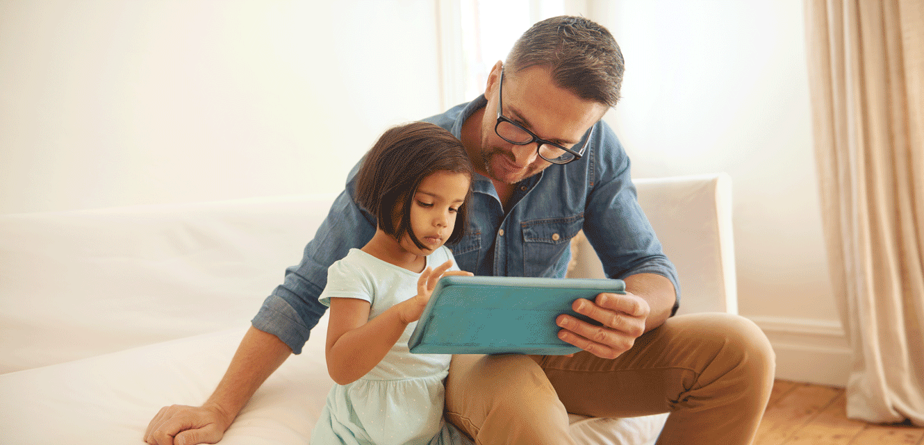 A young girl taps the screen of a tablet computer while her father holds it for her