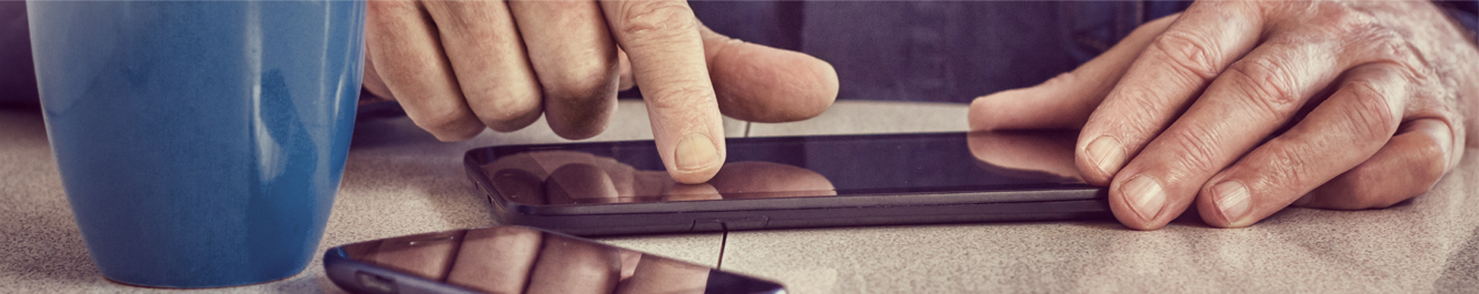 older man touches screen of smartphone while drinking coffee