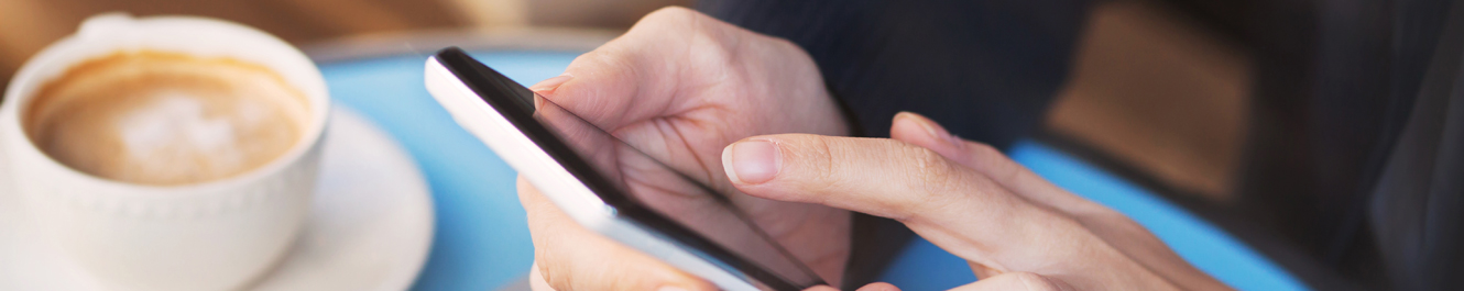 person tapping on a smartphone next to a cup of coffee