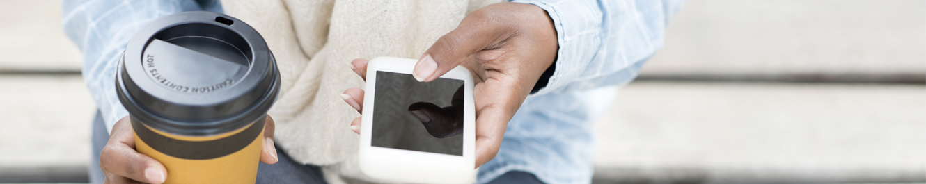 African-American woman sits holding a to-go cup and an iPhone